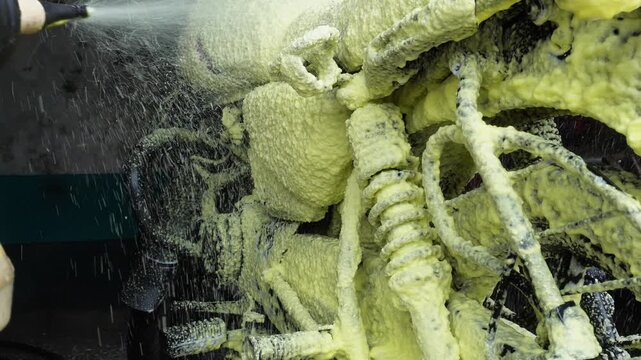 Worker spraying yellow snow foam on motorcycle during wash
