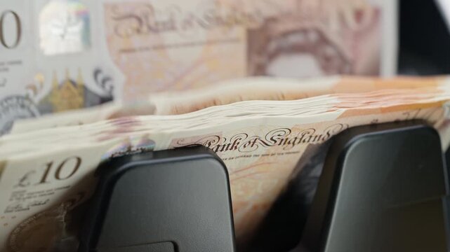 Automatic money counting machine processing 10 GBP British pound banknotes for currency exchange. International finance, travel money and foreign exchange services.