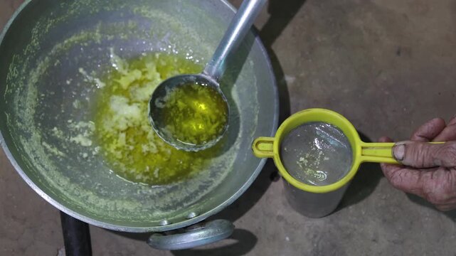 Raw video footage of a village woman straining homemade ghee in a traditional rural kitchen in Uttarakhand, India, showcasing authentic cooking, village life, and poverty.