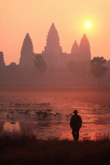 Fototapeta premium Traveler silhouetted against the misty sunrise over Angkor Wat's ancient spires, with lotus ponds in the foreground.