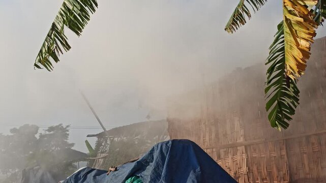 Dense smoke rising from the traditional production of coconut shell charcoal, illustrating the carbonization process, biomass fuel production, and small-scale manufacturing in a rural environment.