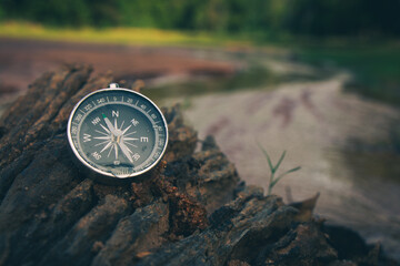 The compass on the rocks by the river in the forest is a symbol of travel. © r_tee