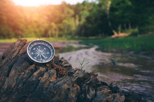 The compass on the rocks by the river in the forest is a symbol of travel.