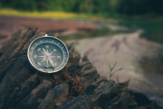 The compass on the rocks by the river in the forest is a symbol of travel.