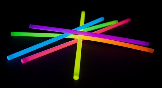 Macro shot of glowing colorful glow sticks crossed together, dark background.