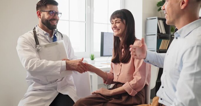 Doctor meets couple for pregnancy consultation. Doctor welcomes parents at clinic, offering healthcare advice and outlining appointment and examination steps. Theme of supportive medical care.
