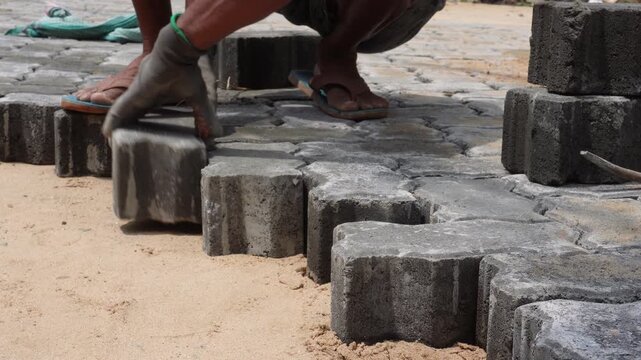 Worker installing interlocking concrete paver blocks on a sand base.