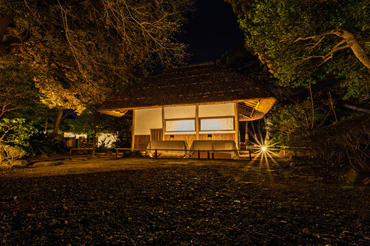 Illuminated historic thatched-roof hut Kuhachi-ya at night in Koishikawa Korakuen Garden January 2024