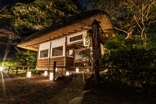 Close up view of the illuminated thatched-roof Kuhachi-ya hut with a paper lantern at Koishikawa Korakuen at night January 2024