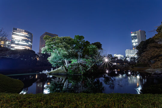 Night view of illuminated Horaijima Island and pond reflection with urban skyscrapers at Koishikawa Korakuen January 2024