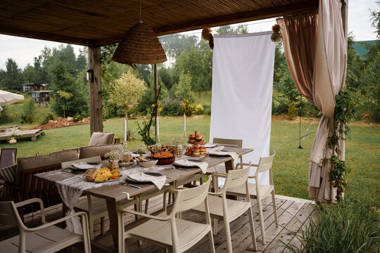 An outdoor dining setup on a wooden table under a gazebo in a lush green garden during summer, perfect for parties and social gatherings, celebration dinner with family and friends