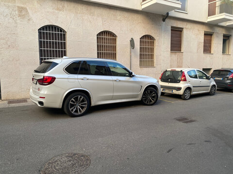 White BMW X5 SUV and compact cars parked on Via Eugenio Beltrami street in Cremona, Lombardy, Italy