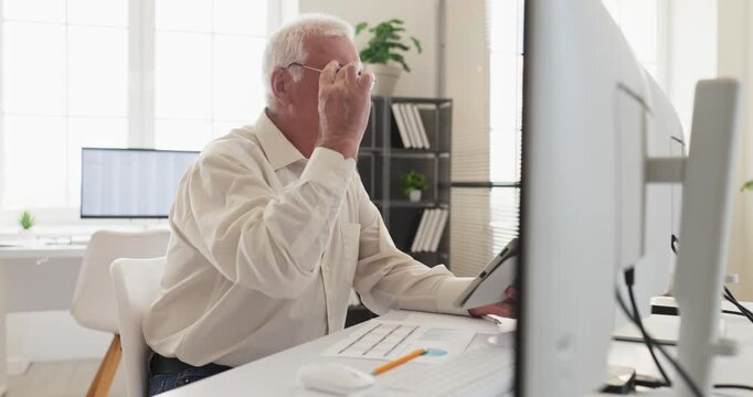 Senior man accountant analyst in office using computer. Documents, charts, and a tablet support finance data review and accurate decision making. Theme is financial analysis and reliability.