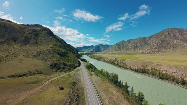 Aerial tracking shot of river and road winding through mountain valley with turquoise water and roadside trees Chuysky tract Altai, Siberia, Russia.