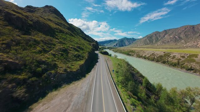 Aerial fpv showing winding turquoise river and adjacent mountain road through rocky valley under blue sky Chuysky tract Altai, Siberia, Russia.