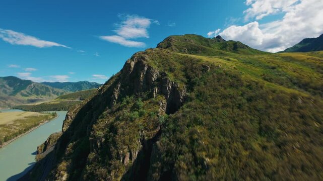 Aerial tracking shot of grassy mountain ridge sweeping over river valley and meadow under blue sky and drifting clouds Chuysky tract Altai, Siberia, Russia.