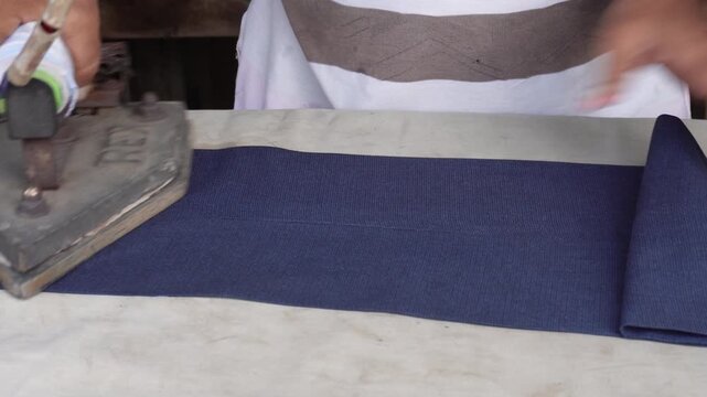 Person pressing dark blue clothing with electric iron