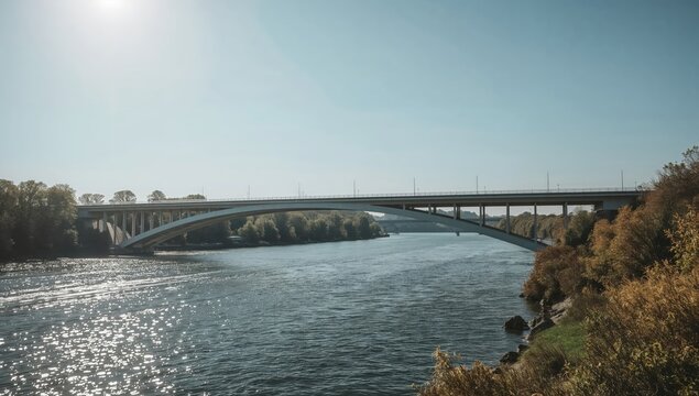 Modern concrete bridge spanning tranquil river with autumn trees and sparkling water under clear blue sky