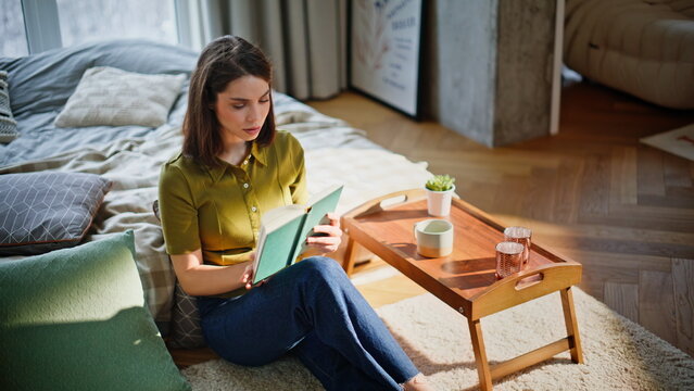 Woman reader holding book sitting floor in bedroom closeup. Dreamy girl resting