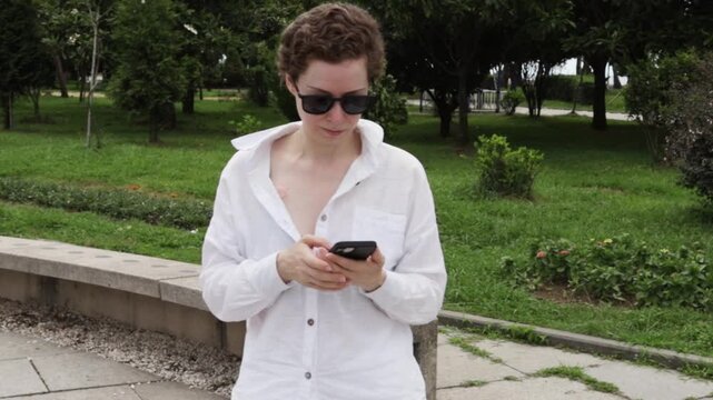 woman in light clothing reads a smartphone in a city plaza, representing electronic health records, telemedicine access and confidence after treatment during an independent city walk
