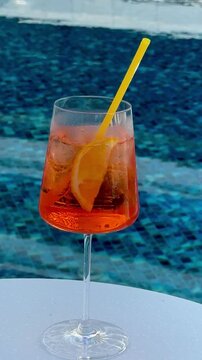 Orange spritz on white poolside table &mdash; turquoise mosaic tiles and sunlit ripples