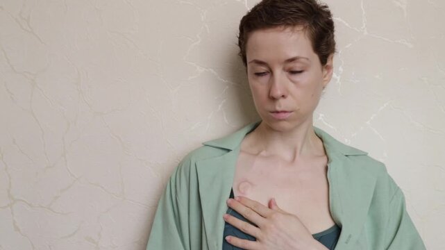 portrait of a woman with a visible port and open overshirt leaning against a wall, expressing survivorship, body confidence and life after chemotherapy
