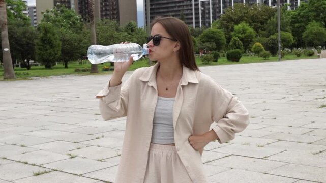 urban teenager holds a water bottle while taking a break in an open plaza, representing heat stress awareness, hydration and summer wellbeing during summer leisure time outdoors