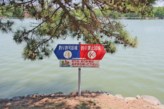Fishing rules sign at Ohori Park Fukuoka, Japan. Fishing allowed and prohibited zones indicated on a directional sign by a park lake