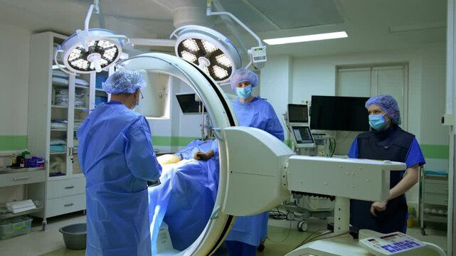 Modern x-ray machine set at the operating table. Surgeon is holding a medical device in his hands.