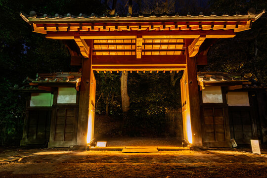 Front view of the historic wooden gate glowing in golden light during the night opening at Koishikawa Korakuen January 2024