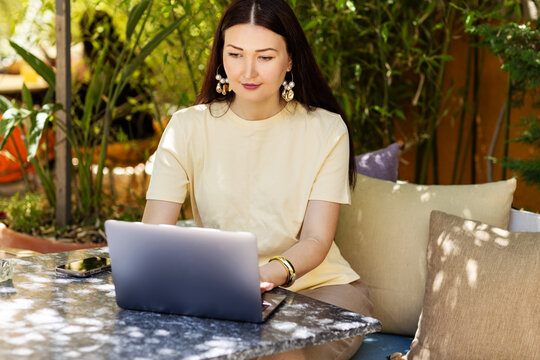 Woman working on laptop in a cafe garden setting