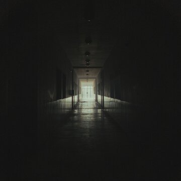 Dark empty hallway with bright exit light at the end. Moody corridor leading to illuminated doorway for dramatic escape or journey scenes.