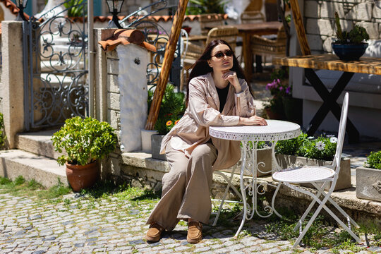Woman relaxing at sunny patio table in rustic courtyard