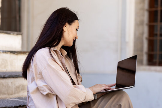 Young woman working on laptop outdoors near building steps