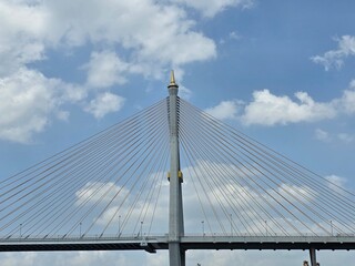 Obraz premium Modern Cable-Stayed Bridge Tower: A majestic tower of a cable-stayed bridge reaching towards a partly cloudy blue sky, showcasing intricate engineering and architectural design.