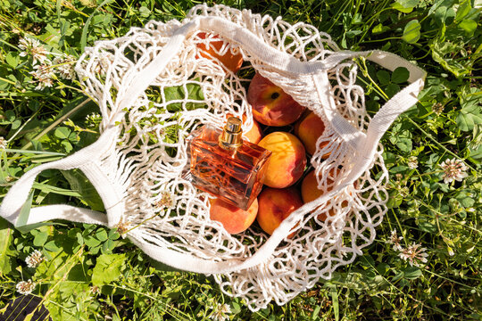Perfume bottle with peach in a net bag on green grass