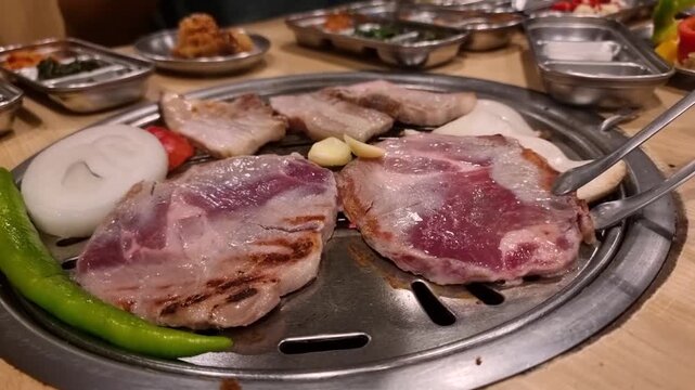 Tongs flipping pork meat on hot grill plate in Korean BBQ restaurant