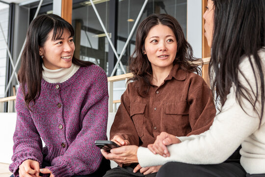 Japanese friends chatting in cafe with smartphone during break