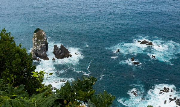 serene rock formations in the ocean with lush vegetation and dynamic waves crashing against the cliffs from an aerial view above the cliffs during a peaceful coastal.