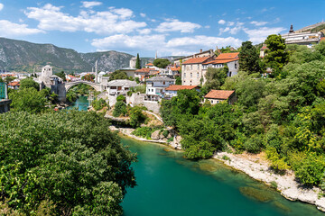 Naklejka premium Mostar in Bosnia and Herzegovina with the turquoise Neretva River, green hills, traditional houses and mountain scenery captured on a bright summer day.
