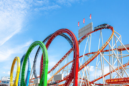 Roller coaster riders travel across brightly colored curved tracks beneath a clear blue sky, forming an energetic amusement park image with speed, adventure and excitement.