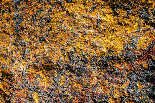 Natural stone surface with vivid yellow, orange and gray mineral tones creates an abstract rugged texture for backgrounds, branding, graphic design and creative visual projects.