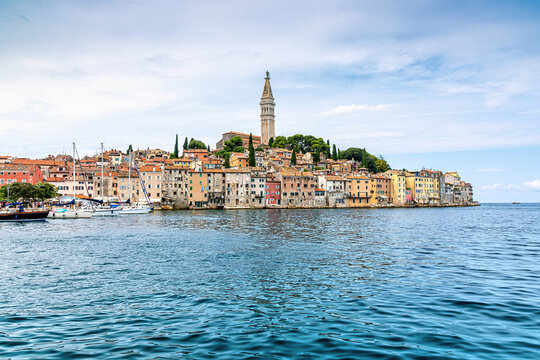 Rovinj, Croatia, with colorful old town buildings, church tower, boats and calm Adriatic Sea in a scenic summer waterfront view.