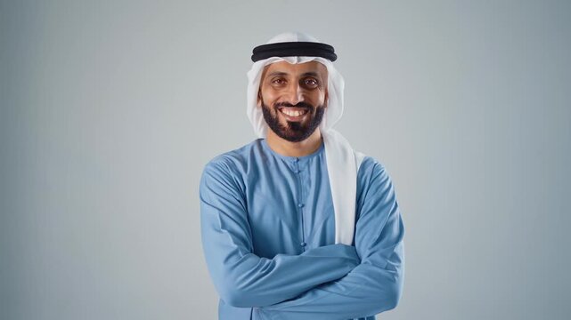 Confident young arab man with a beard wearing traditional clothing, a keffiyeh and agal, looking at the camera and smiling, expressing happiness and success on a gray studio background