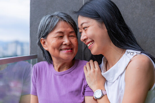 Joyful Asian mother and adult daughter smiling on balcony