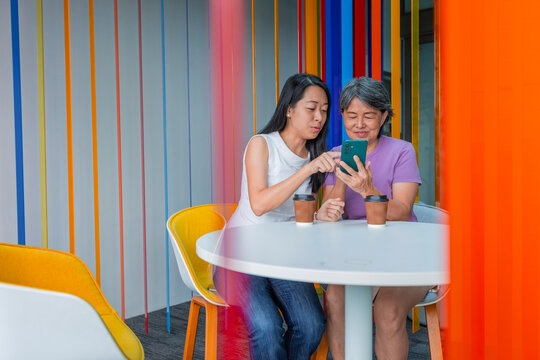 Senior Asian mum and daughter using smartphone in cafe