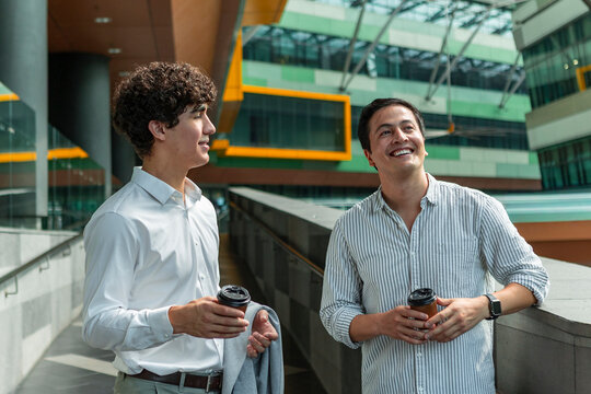 Two colleagues chatting with coffee in modern office atrium