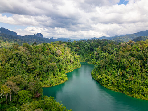 Aerial view of hilly forested waterway in Cheow Lan Lake on quiet overcast morning with evergreen lush trees and reflective blue tranquil waters in Khao Sok National Park, Thailand