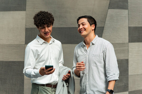 Two young men sharing a smartphone and laughing outdoors