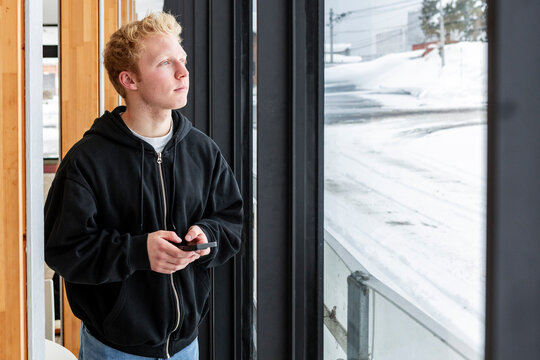 Student taking a break by window, holding smartphone